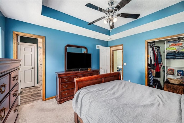 bedroom with a closet, baseboards, light carpet, a ceiling fan, and a tray ceiling