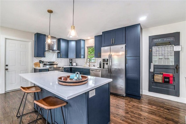 kitchen featuring stainless steel appliances, wall chimney exhaust hood, blue cabinetry, and dark wood-style floors