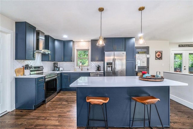 kitchen featuring stainless steel appliances, wall chimney exhaust hood, a breakfast bar area, and blue cabinets