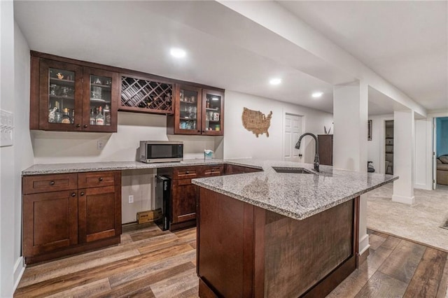 kitchen featuring stainless steel microwave, a sink, wood finished floors, glass insert cabinets, and light stone counters
