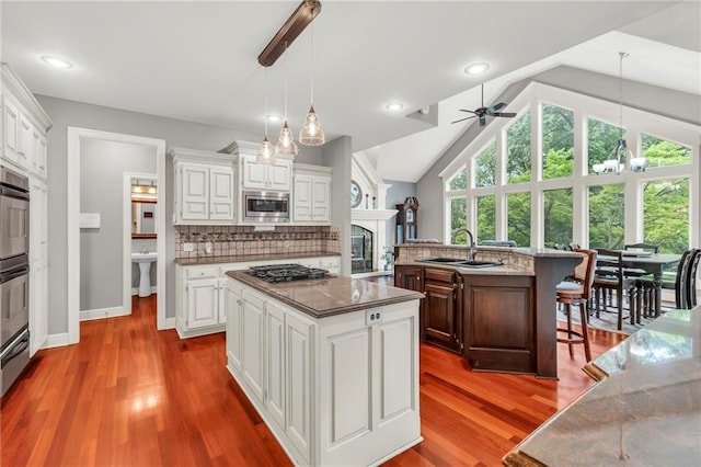 8129 Clearwater Pt, Parkville, MO 64152 - kitchen with stainless steel microwave, an island with sink, gas cooktop, ceiling fan, and a fireplace