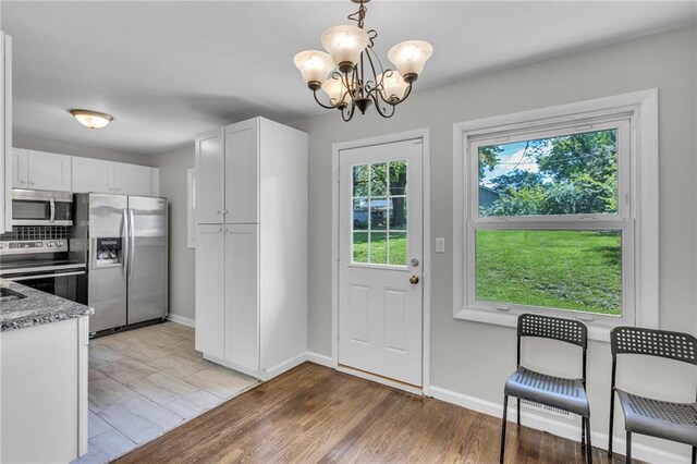 4203 E 113th St, Kansas City, MO 64137 - kitchen featuring appliances with stainless steel finishes, a chandelier, white cabinetry, stone counters, and baseboards
