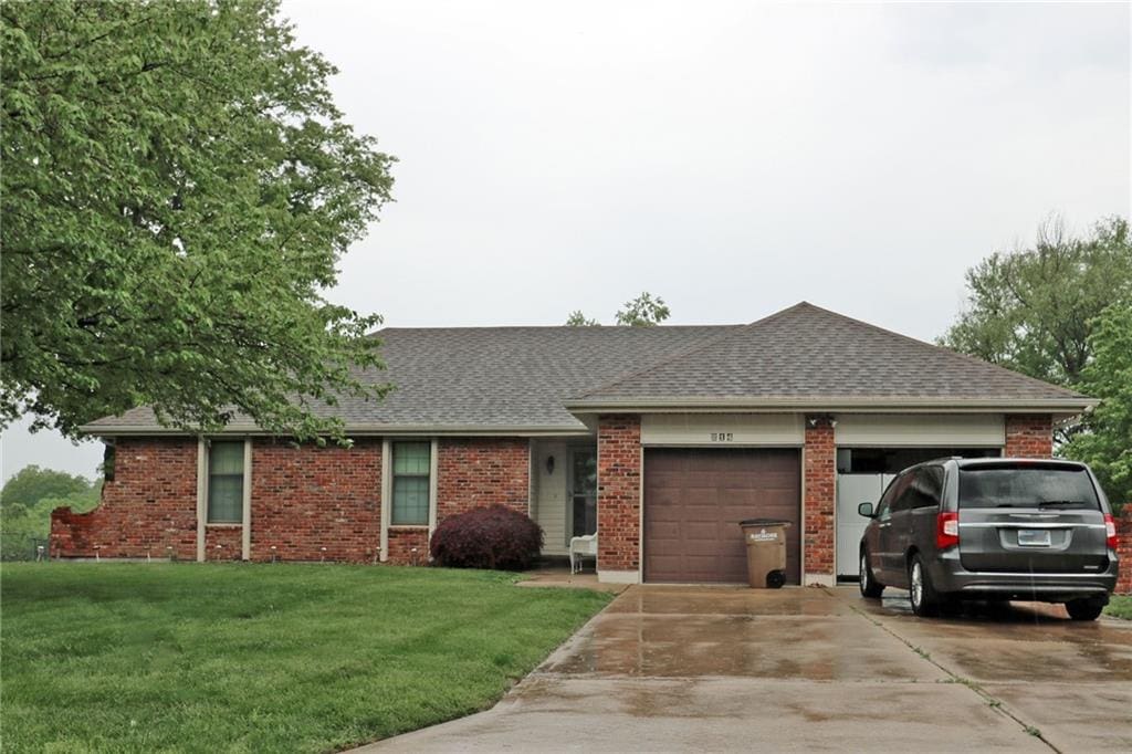 214 Johnston Pkwy, Raymore, MO 64083 - single story home featuring a garage, driveway, a front lawn, brick siding, and a shingled roof