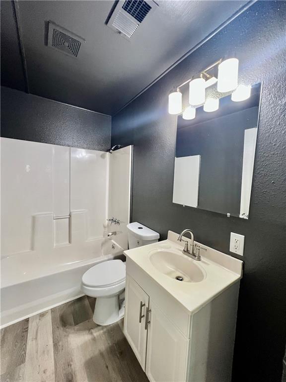 8416 Greenwood Rd, Raytown, MO 64138 - bathroom with a textured wall, wood finished floors, bathtub / shower combination, toilet, and vanity