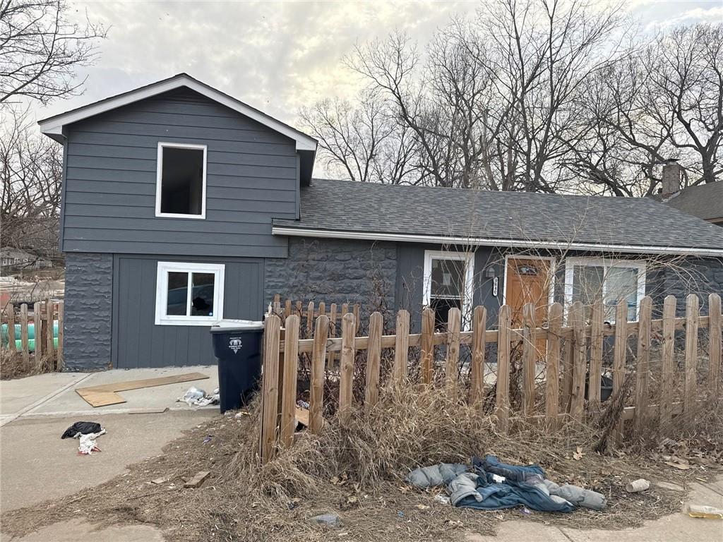 3840 Askew Ave, Kansas City, MO 64128 - view of front facade with stone siding, fence, and a shingled roof
