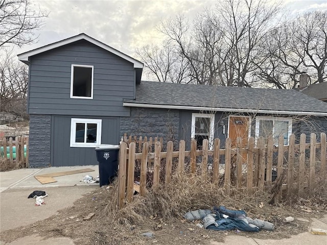 view of front facade with stone siding, fence, and a shingled roof