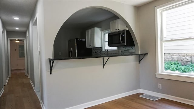 2243 Spruce Ave, Kansas City, MO 64127 - kitchen featuring stainless steel microwave, fridge, dark countertops, wood finished floors, and recessed lighting