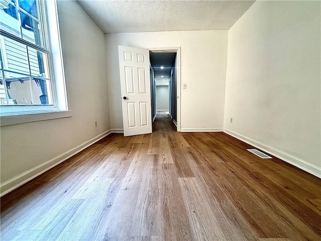 2243 Spruce Ave, Kansas City, MO 64127 - unfurnished bedroom with wood finished floors, baseboards, multiple windows, and a textured ceiling