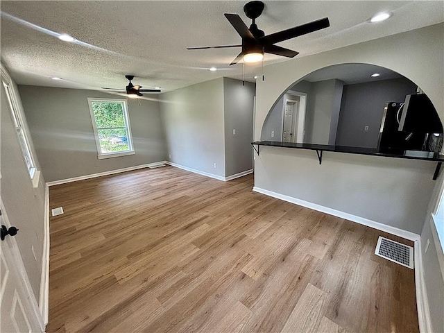 2243 Spruce Ave, Kansas City, MO 64127 - unfurnished living room with a ceiling fan, light wood-style flooring, arched walkways, baseboards, and a textured ceiling