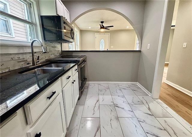 2243 Spruce Ave, Kansas City, MO 64127 - kitchen with stainless steel appliances, baseboards, a sink, arched walkways, and light marble finish flooring