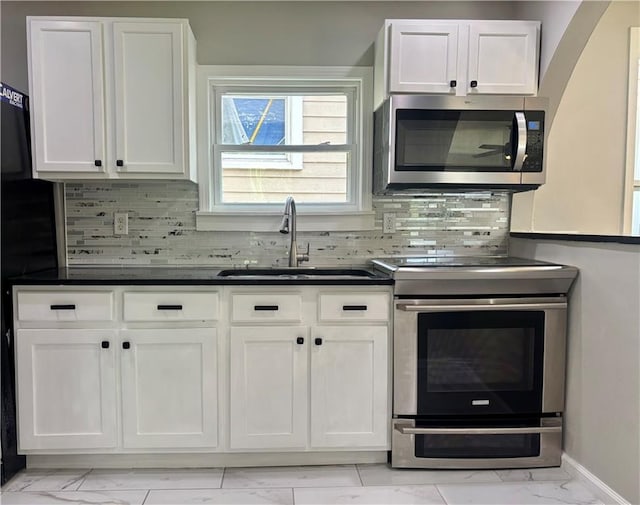 2243 Spruce Ave, Kansas City, MO 64127 - kitchen featuring stainless steel appliances, light marble finish floors, a sink, white cabinets, and dark countertops