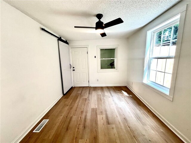 2243 Spruce Ave, Kansas City, MO 64127 - empty room with a barn door, wood finished floors, baseboards, a textured ceiling, and ceiling fan