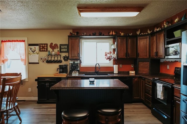 7164 State Route T Hwy, Amazonia, MO 64421 - kitchen featuring black / electric stove, a sink, stainless steel microwave, a center island, and light wood-style floors