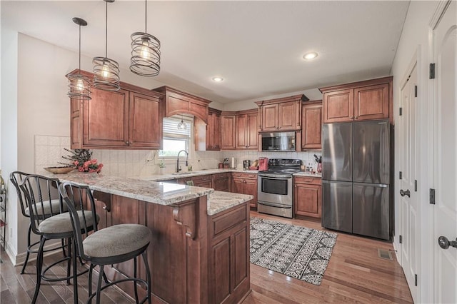 kitchen featuring appliances with stainless steel finishes, a sink, a peninsula, brown cabinetry, and wood finished floors
