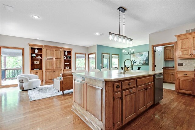 6330 N Nevada Ave, Parkville, MO 64152 - kitchen featuring stainless steel dishwasher, a sink, wood finished floors, light countertops, and a center island with sink
