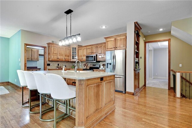 6330 N Nevada Ave, Parkville, MO 64152 - kitchen with appliances with stainless steel finishes, light countertops, a kitchen island with sink, light wood-style flooring, and a breakfast bar area