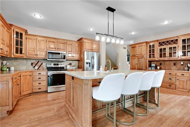 6330 N Nevada Ave, Parkville, MO 64152 - kitchen featuring appliances with stainless steel finishes, light countertops, a center island with sink, light wood-type flooring, and a breakfast bar area