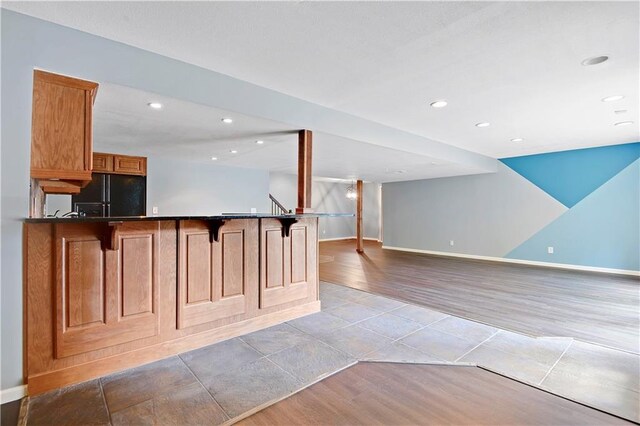 6330 N Nevada Ave, Parkville, MO 64152 - kitchen with freestanding refrigerator, wood finished floors, dark countertops, a breakfast bar area, and brown cabinets