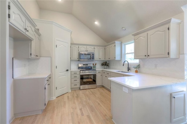1102 Manse Dr, Raymore, MO 64083 - kitchen with stainless steel appliances, a sink, a peninsula, vaulted ceiling, and light wood-type flooring
