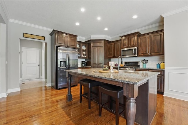 17311 Blue Moon Ln, Tonganoxie, KS 66086 - kitchen with stainless steel appliances, a breakfast bar, dark brown cabinetry, light wood-style floors, and light stone counters