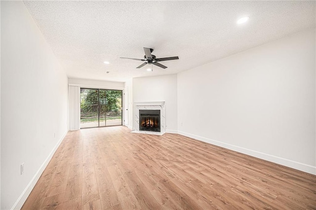 unfurnished living room with a textured ceiling, light wood-type flooring, ceiling fan, a fireplace with flush hearth, and baseboards