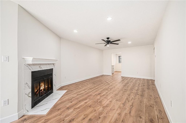 unfurnished living room featuring a high end fireplace, light wood-style flooring, a ceiling fan, recessed lighting, and baseboards