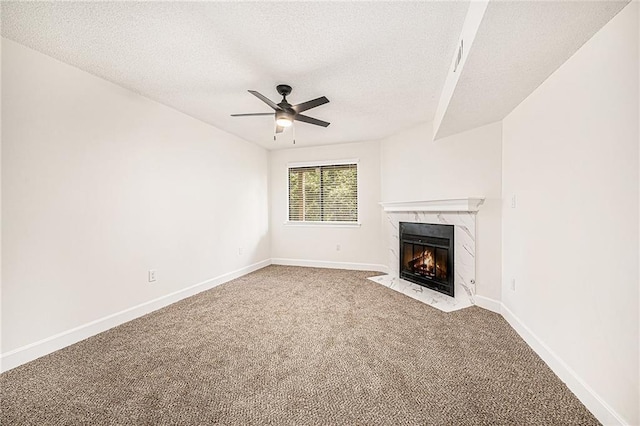 unfurnished living room with carpet flooring, a ceiling fan, a textured ceiling, a high end fireplace, and baseboards