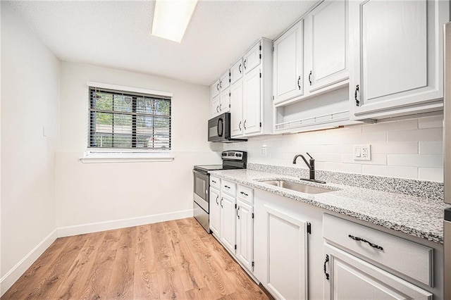 kitchen featuring stainless steel electric range oven, a sink, backsplash, light stone countertops, and baseboards