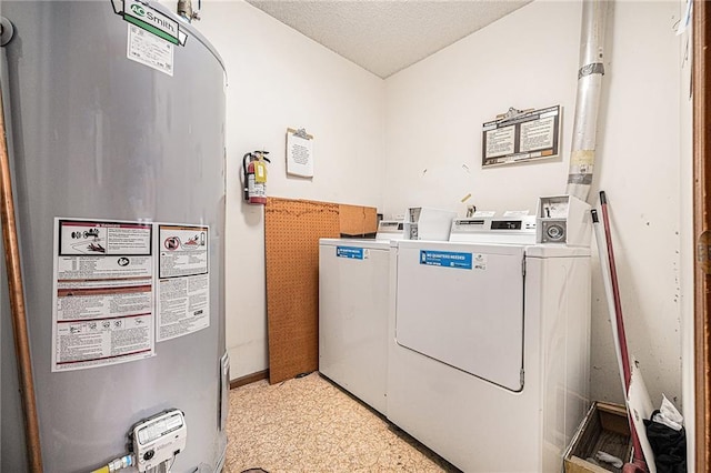 washroom with water heater, washing machine and clothes dryer, a textured ceiling, and baseboards
