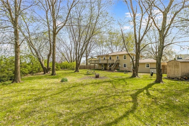 view of green lawn with stairway, a deck, a shed, and an outbuilding