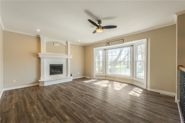 unfurnished living room featuring a ceiling fan, baseboards, dark wood-style flooring, ornamental molding, and a fireplace