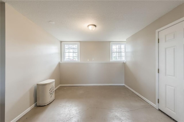 empty room with concrete floors, plenty of natural light, baseboards, and a textured ceiling