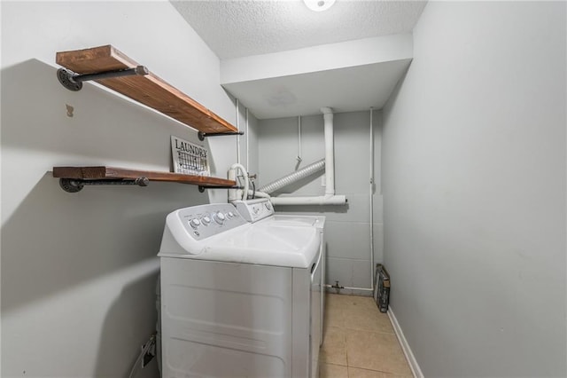 laundry room featuring washer and dryer, a textured ceiling, light tile patterned floors, and baseboards