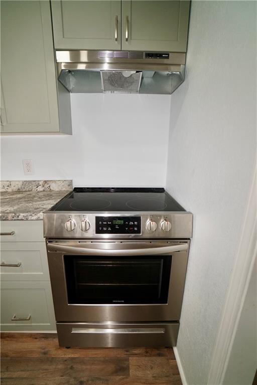 kitchen with stainless steel electric range, under cabinet range hood, dark wood finished floors, white cabinets, and light stone counters
