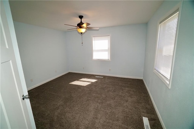 spare room with dark colored carpet, ceiling fan, and baseboards