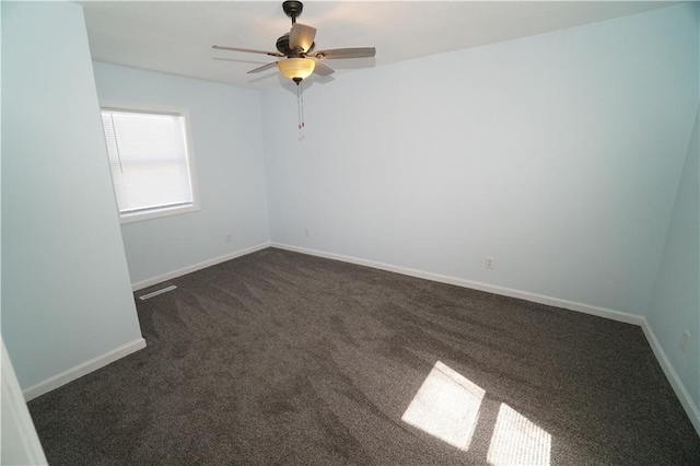 spare room featuring dark colored carpet, ceiling fan, and baseboards
