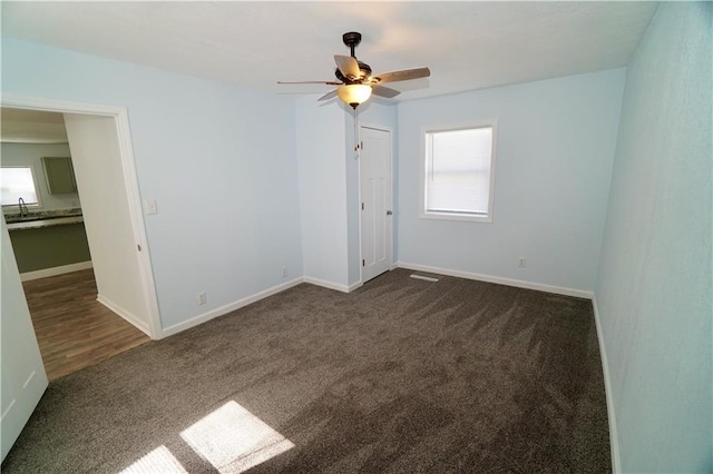 spare room with dark carpet, a ceiling fan, a sink, and baseboards