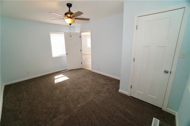 spare room with dark colored carpet, ceiling fan, and baseboards