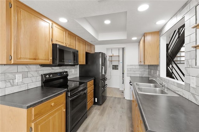 kitchen featuring black appliances, a sink, a tray ceiling, light wood-style floors, and dark countertops