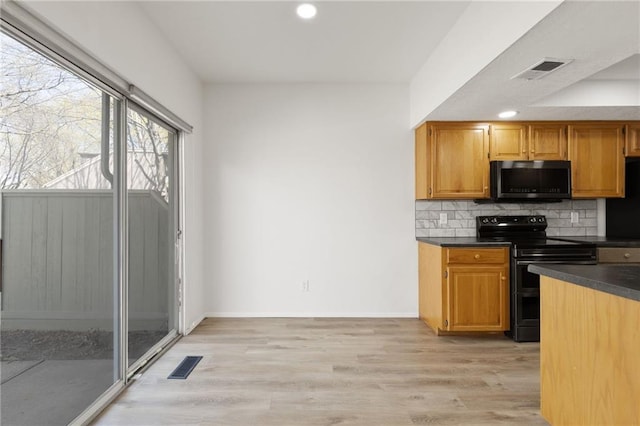 kitchen with black range with electric stovetop, stainless steel microwave, dark countertops, decorative backsplash, and light wood finished floors