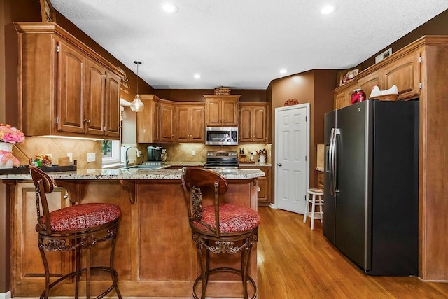9008 N Hunter Ave, Kansas City, MO 64157 - kitchen with stainless steel appliances, a peninsula, light wood-style flooring, decorative backsplash, and brown cabinets