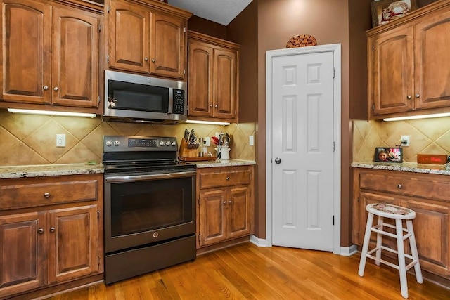 9008 N Hunter Ave, Kansas City, MO 64157 - kitchen with appliances with stainless steel finishes, light wood-style flooring, decorative backsplash, light stone countertops, and brown cabinets