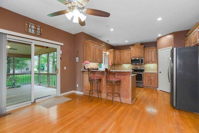 9008 N Hunter Ave, Kansas City, MO 64157 - kitchen with stainless steel appliances, a peninsula, light wood-style floors, a kitchen bar, and tasteful backsplash