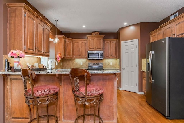 9008 N Hunter Ave, Kansas City, MO 64157 - kitchen with appliances with stainless steel finishes, a peninsula, light wood finished floors, brown cabinetry, and backsplash