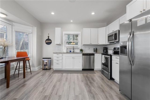915 E 29th St, Kansas City, MO 64109 - kitchen featuring appliances with stainless steel finishes, light stone counters, white cabinets, backsplash, and light wood-type flooring