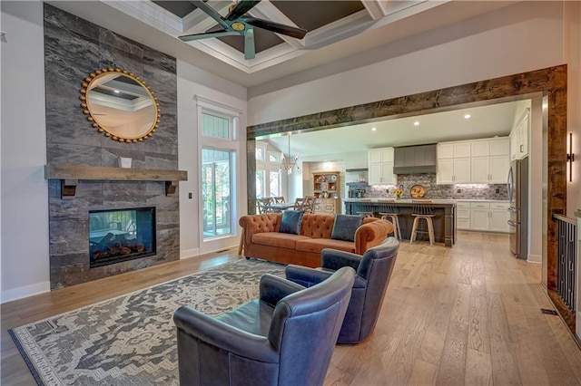 living area featuring a ceiling fan, light wood-style flooring, a high ceiling, beam ceiling, and a multi sided fireplace