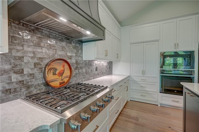 kitchen featuring appliances with stainless steel finishes, premium range hood, light wood finished floors, white cabinetry, and tasteful backsplash