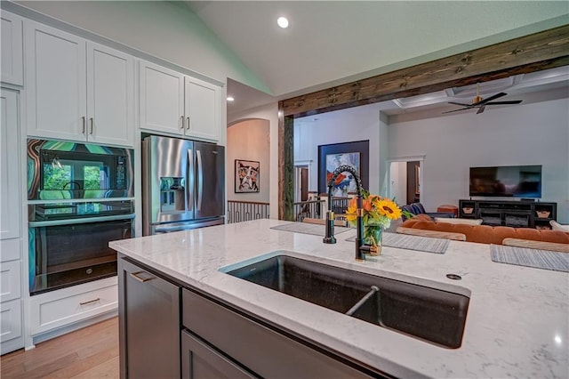 kitchen featuring black appliances, a sink, light stone counters, lofted ceiling, and light wood finished floors
