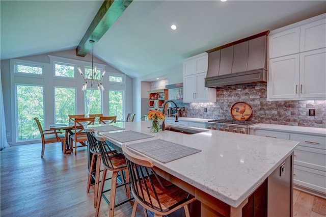 kitchen with a sink, custom range hood, light wood-style floors, and tasteful backsplash