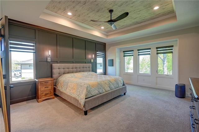 bedroom with a tray ceiling, light colored carpet, recessed lighting, ceiling fan, and crown molding